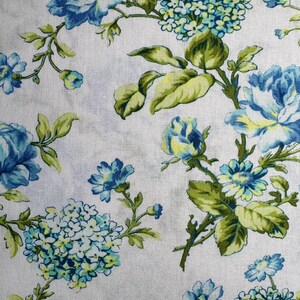 K&ouml;nnte beinhalten: Blumenstoff mit blauen und wei&szlig;en Blumen, gr&uuml;nen Bl&auml;ttern und Stielen. Das Design umfasst gro&szlig;e Rosen und kleinere Bl&uuml;tencluster, die ein Muster auf wei&szlig;em Hintergrund bilden.