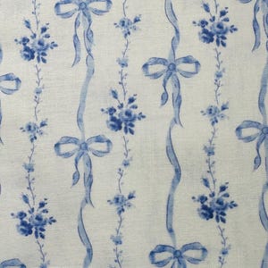 May include: A fabric with a repeating pattern of blue ribbons, bows, and floral bouquets on a white background. The design features vertical ribbons with bows and floral clusters, creating a delicate and classic aesthetic.