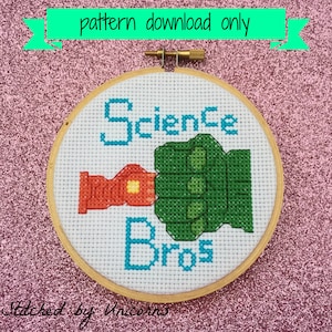 May include: A white embroidery hoop with a cross-stitch design of two fists bumping, one red and one green, with the text "Science Bros" in blue lettering.