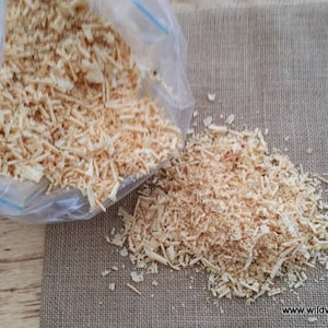 May include: A clear plastic bag filled with wood shavings, with more shavings spilling out onto a brown hessian surface.