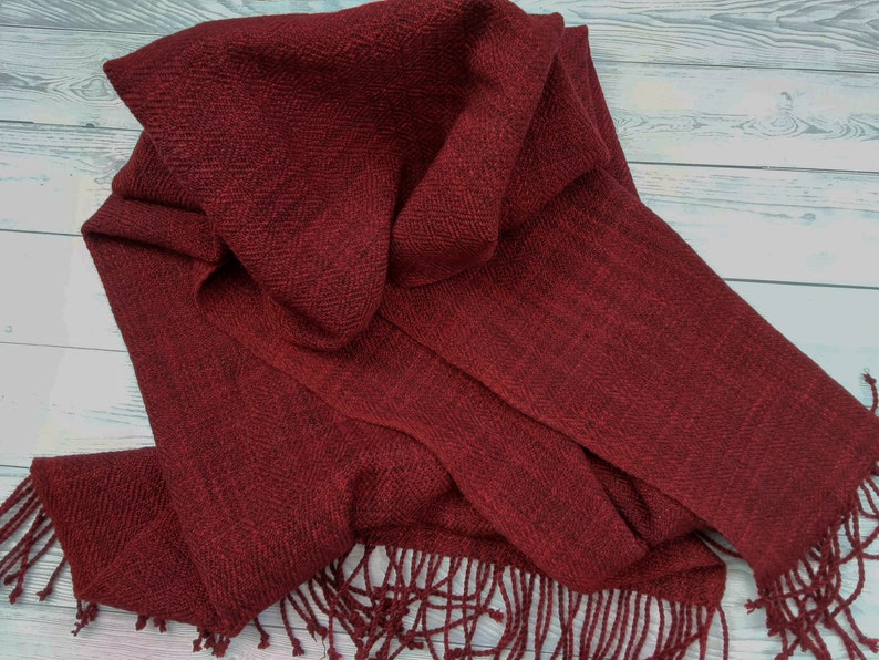 Puede incluir: Una bufanda de color rojo oscuro con un patr&oacute;n de espiga y flecos en los extremos.