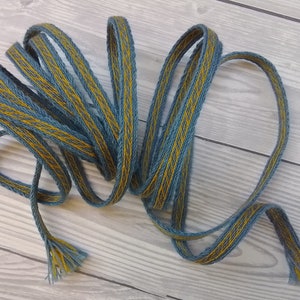 May include: A woven blue and yellow ribbon with a textured pattern. The ribbon is coiled and has frayed ends.