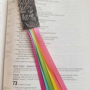 May include: A close-up of an open Bible with a bookmark and a rainbow ribbon. The Bible is open to Psalm 73, which reads "Truly God is good to Israel, to those whose hearts are pure."