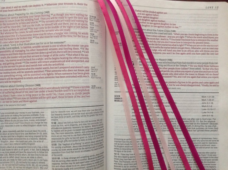 Może przedstawiać: Otwartą Biblia z r&oacute;żowymi i białymi wstążkami jako zakładkami. Tekst na stronie brzmi: "Gdzie jest tw&oacute;j skarb, tam będzie też twoje serce." Biblia jest otwarta na Ewangelię według św. Łukasza, rozdział 13.