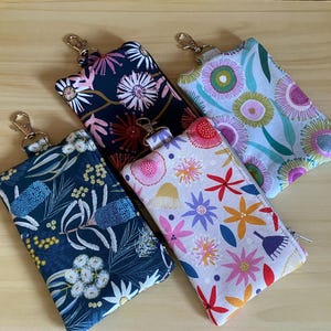 May include: Four small, zippered pouches with key rings, each with a unique floral design. The patterns include a dark blue background with white and yellow flowers, and a light background with colourful flowers.