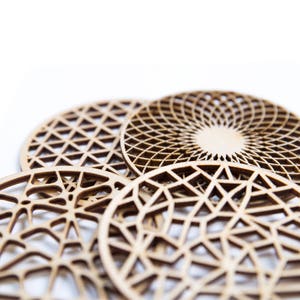 Op de afbeelding: Vier houten onderzetters met ingewikkelde geometrische ontwerpen. De onderzetters zijn gemaakt van lichtbruin hout en hebben een ronde vorm.