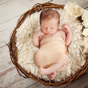 Pu&ograve; includere: Un neonato dorme pacificamente in un cesto di vimini rivestito di pelliccia bianca. Il bambino &egrave; avvolto in un fasciatoio beige e circondato da fiori bianchi.