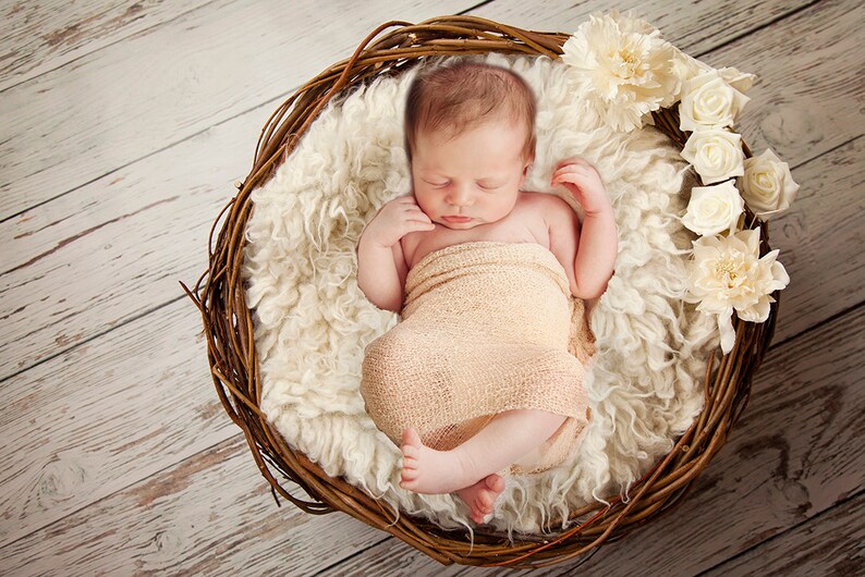 Pu&ograve; includere: Un neonato dorme pacificamente in un cesto di vimini rivestito di pelliccia bianca. Il bambino &egrave; avvolto in un fasciatoio beige e circondato da fiori bianchi.