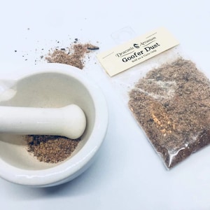 May include: A white ceramic mortar and pestle with a brown powder inside. A small plastic bag with a label that reads "Draconis Arcanum Goofer Dust Sold as a Curio Only" contains a brown powder.