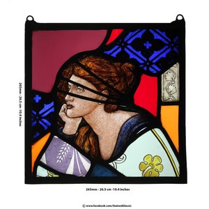 May include: Stained glass panel featuring a woman with auburn hair, resting her chin on her hand. The artwork includes red, blue, orange, and white glass, with a black border. The panel measures 10.4 inches in height and width.
