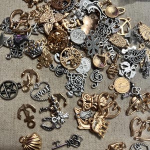 May include: A collection of silver and gold charms featuring various designs, including anchors, hearts, crowns, trees, and keys. The charms are perfect for jewelry making or adding a personal touch to crafts.