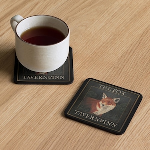 May include: Two black square coasters with a gold border and the text "Tavern & Inn" printed on them. One coaster features a red fox with the text "The Fox" above it.