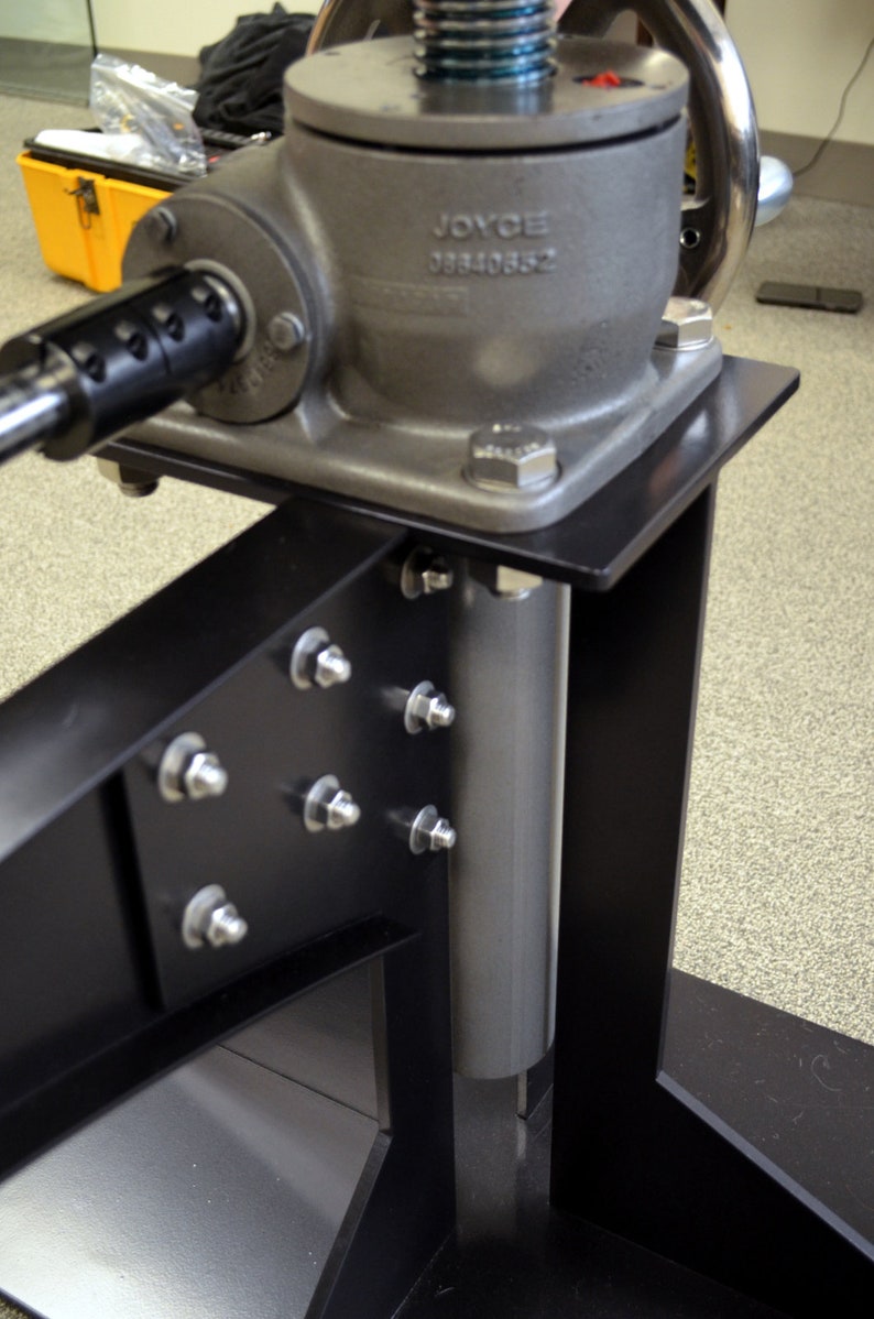 May include: A black metal stand with a silver metal cylinder and a silver metal gear mechanism. The gear mechanism has a black handle and a label that reads "JOYCE 08840882".