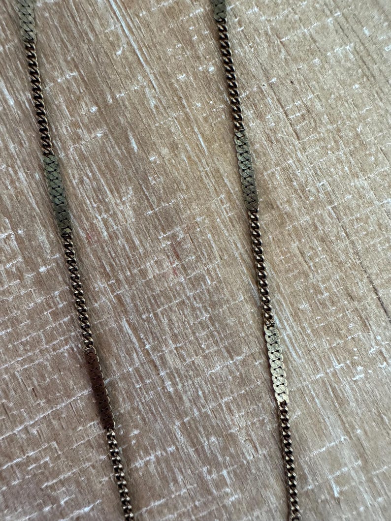 Puede incluir: Primer plano de dos collares dorados con un dise&ntilde;o de cadena rectangular texturizada. Los collares se muestran sobre una superficie de madera marr&oacute;n claro. Las cadenas tienen una apariencia delicada y vintage.