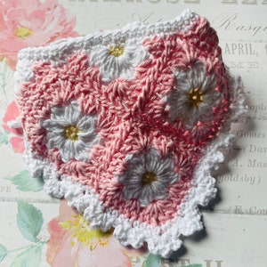 Op de afbeelding: Een geh&auml;keld vierkant met een roze en wit bloemenpatroon en een witte gehaakte rand. Het vierkant is gemaakt met een granny stitch-patroon.