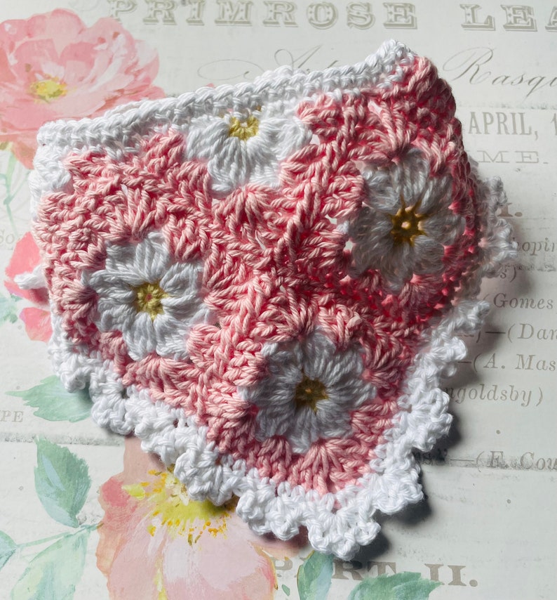 Op de afbeelding: Een geh&auml;keld vierkant met een roze en wit bloemenpatroon en een witte gehaakte rand. Het vierkant is gemaakt met een granny stitch-patroon.