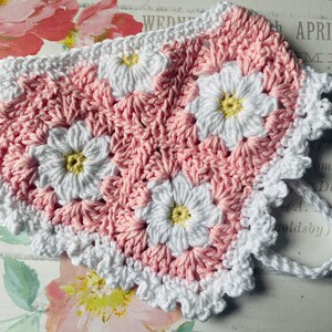 Op de afbeelding: Een roze en wit geh&auml;keld hartvormig stuk met een witte geh&auml;kelde rand. Het stuk is gemaakt van kleine bloemen met gele centra.