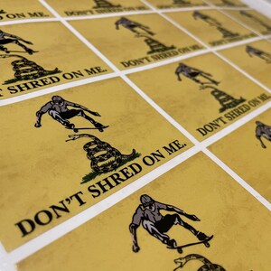 K&ouml;nnte beinhalten: Ein Bogen Aufkleber mit gelbem Hintergrund. Jeder Aufkleber zeigt einen Skater, eine zusammengerollte Schlange und den Text "DON'T SHRED ON ME." Der Skater ist in Bewegung, und die Schlange ist gr&uuml;n und braun. Die Aufkleber sind in einem Raster angeordnet.