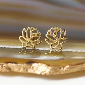May include: A pair of gold-toned lotus flower stud earrings. The earrings are delicate and intricate, with a cutout design.