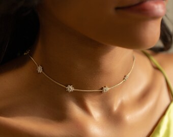 May include: A gold chain choker necklace with small flower-shaped charms set with clear stones.
