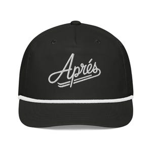 Puede incluir: Una gorra de béisbol negra con el texto "Après" bordado en blanco en el panel frontal. La gorra incluye un detalle de cuerda trenzada blanca que recorre horizontalmente la base de la corona, justo encima de la visera curva.