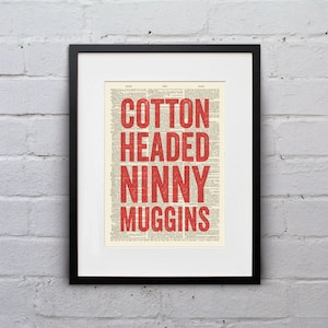 Puede incluir: Una impresión enmarcada de la frase "Cotton Headed Ninny Muggins" en texto rojo sobre un fondo de página de diccionario vintage.