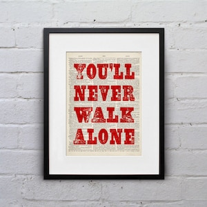 Könnte beinhalten: Ein gerahmter Druck mit dem Text "You'll Never Walk Alone" in roten Buchstaben auf einem Vintage-Zeitungspapier-Hintergrund.