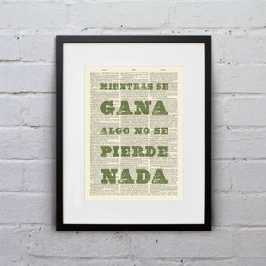 May include: A framed print with a black frame, featuring text in green over a vintage dictionary page background. The text reads "Mientras se gana algo no se pierde nada."