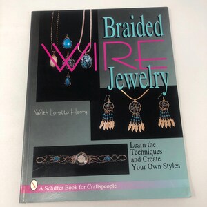 May include: A softcover book titled Braided Wire Jewelry with Loretta Henry. The cover features photographs of wire-wrapped necklaces, earrings, and a watch on a black background. The text reads Learn the Techniques and Create Your Own Styles.