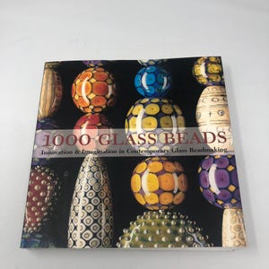 May include: A book titled "1000 Glass Beads" with colorful glass bead designs on the cover. The beads are various shapes and colors, including orange, yellow, blue, and green, against a black background.