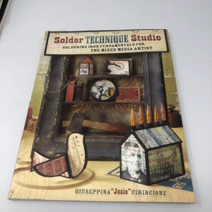 May include: A softcover book titled Solder Technique Studio: Soldering Iron Fundamentals for the Mixed Media Artist by Giuseppina Josie Cirincione. The cover features a collage of soldered art pieces, including a bird, a house, and tools.