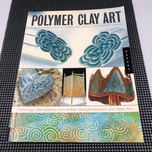 May include: A book titled "POLYMER CLAY ART" with images of polymer clay projects. The cover features examples of jewelry, figures, and decorative surfaces. The book's authors are Celie Fago, Ellen Marshall, Livia McRee, Georgia Sargeant, and Dinko Tilov.