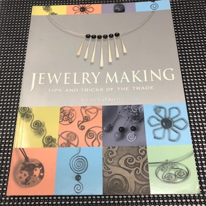 May include: A book titled "JEWELRY MAKING" with the subtitle "TIPS AND TRICKS OF THE TRADE" by Stephen O'Keefe. The cover features a silver necklace design with black beads and gold-colored bars, and various jewelry designs in colorful squares.