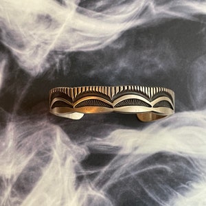 May include: A silver bracelet with a geometric design. The bracelet is made of sterling silver and has a polished finish.
