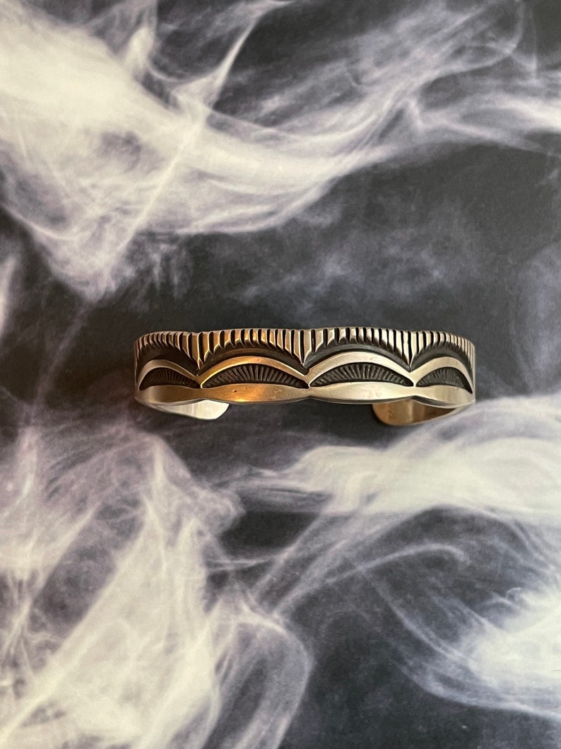 May include: A silver bracelet with a geometric design. The bracelet is made of sterling silver and has a polished finish.