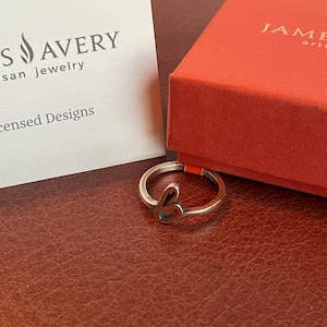 May include: A silver ring with the letter "b" in a cursive font. The ring is next to a red box and a white card with the "S Avery" logo. The background is a brown leather surface.