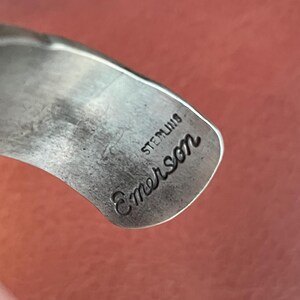 K&ouml;nnte beinhalten: Nahaufnahme eines silbernen Armbands mit der Gravur "Sterling Emerson".