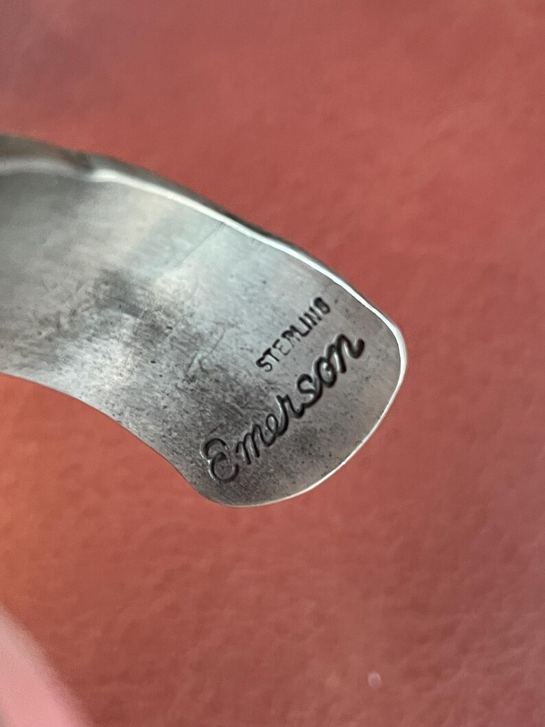 K&ouml;nnte beinhalten: Nahaufnahme eines silbernen Armbands mit der Gravur "Sterling Emerson".