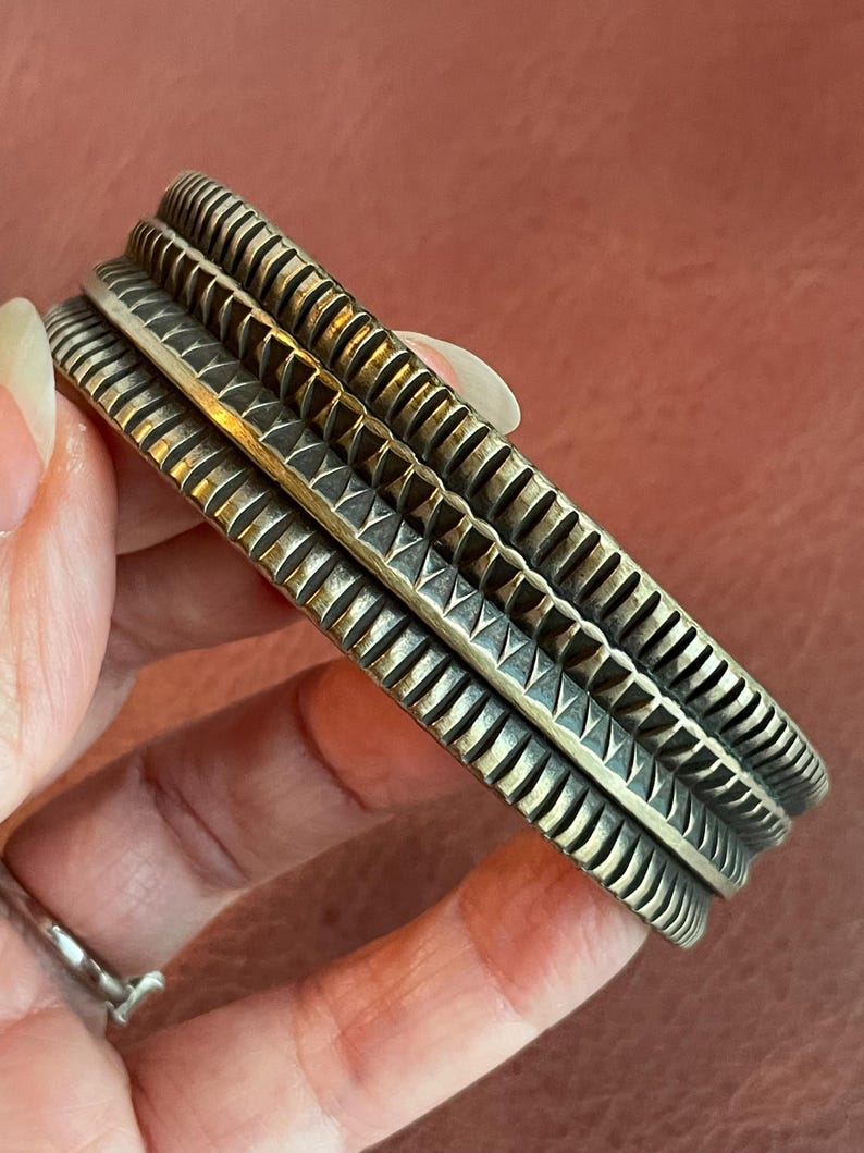 K&ouml;nnte beinhalten: Ein silbernes Armband mit geometrischem Muster. Das Armband besteht aus zwei B&auml;ndern mit einer strukturierten Oberfl&auml;che.