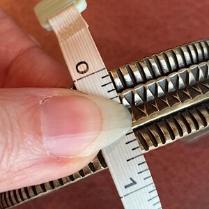 K&ouml;nnte beinhalten: Ein silbernes Armband mit einem strukturierten Design, gemessen mit einem Ma&szlig;band, das eine L&auml;nge von 2,5 cm anzeigt.