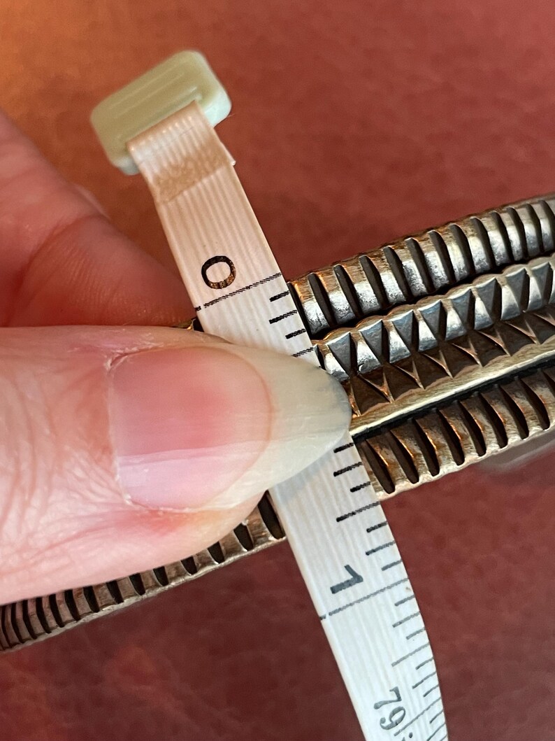 K&ouml;nnte beinhalten: Ein silbernes Armband mit einem strukturierten Design, gemessen mit einem Ma&szlig;band, das eine L&auml;nge von 2,5 cm anzeigt.