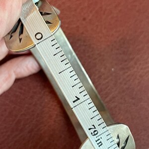 K&ouml;nnte beinhalten: Ein silbernes Armband mit einem dekorativen Design. Das Armband wird mit einem Lineal gemessen und hat einen Durchmesser von 5 cm.