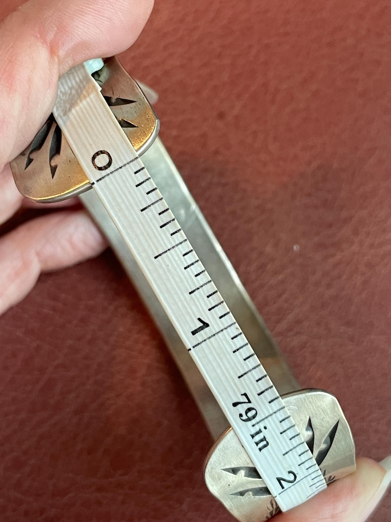 K&ouml;nnte beinhalten: Ein silbernes Armband mit einem dekorativen Design. Das Armband wird mit einem Lineal gemessen und hat einen Durchmesser von 5 cm.