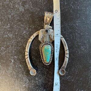 May include: A silver pendant featuring a turquoise stone and a bird motif. The pendant measures approximately 7.6 cm in length. It has a horseshoe shape with floral details at the ends.