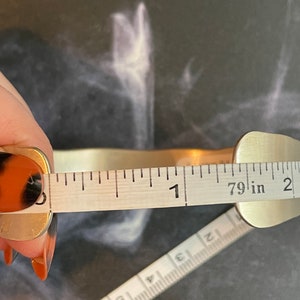 May include: A silver metal bracelet being measured with a tape measure. The tape measure reads 1 7/9 inches.