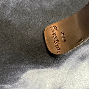 May include: Close-up of a silver bracelet with the inscription "Emmon's Sterling" on the inside.