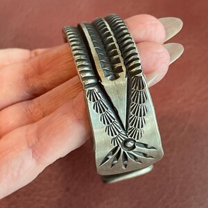 K&ouml;nnte beinhalten: Ein silbernes Armband mit komplizierten geometrischen Mustern. Das Armband besteht aus einem einzigen St&uuml;ck Metall und hat eine glatte, polierte Oberfl&auml;che.