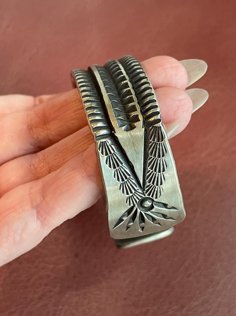 K&ouml;nnte beinhalten: Ein silbernes Armband mit komplizierten geometrischen Mustern. Das Armband besteht aus einem einzigen St&uuml;ck Metall und hat eine glatte, polierte Oberfl&auml;che.