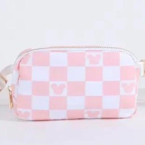 May include: A pink and white checkered fanny pack with a gold zipper and a gold buckle. The fanny pack has a white strap and features a small pink Mickey Mouse silhouette repeated throughout the design.