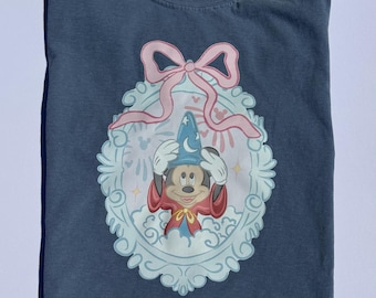 May include: A blue t-shirt with a graphic of Mickey Mouse dressed as a magician in a blue and red robe, with a pink bow and a blue and white ornate frame. The text "Disney's Colors" is on the tag.